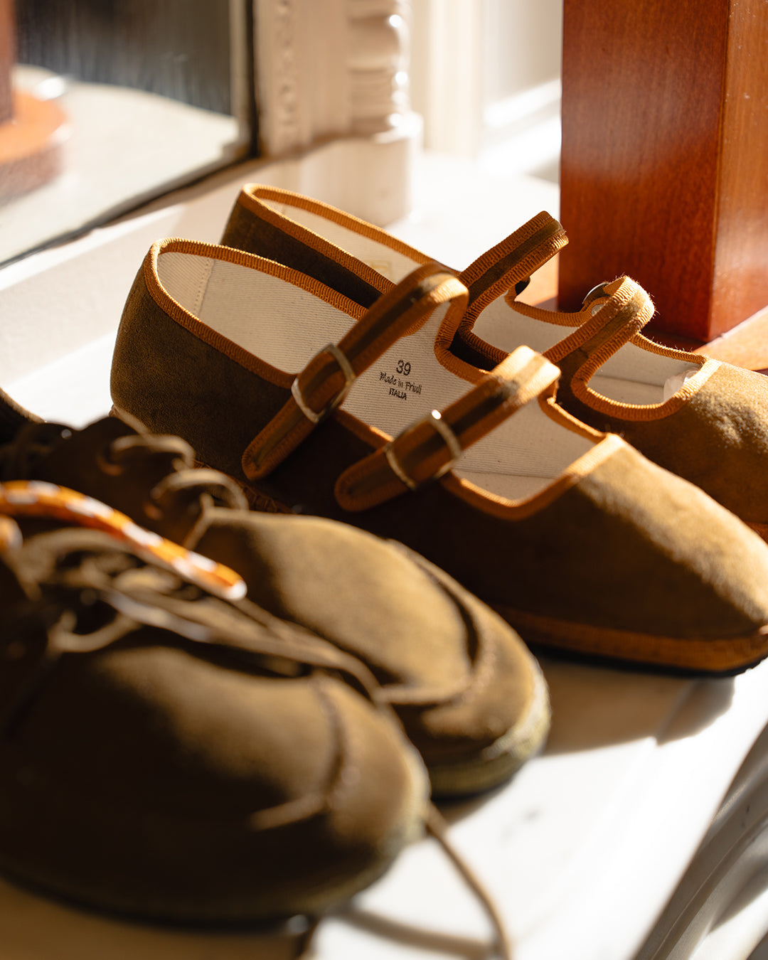Olive Scarpa da Barca next to the Nocciola Double Mary Jane on a sunlit windowsill