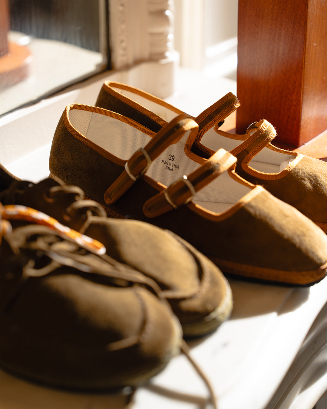 Nocciola Double Mary Jane next to the Olive Scarpa da Barca on a sunlit windowsill
